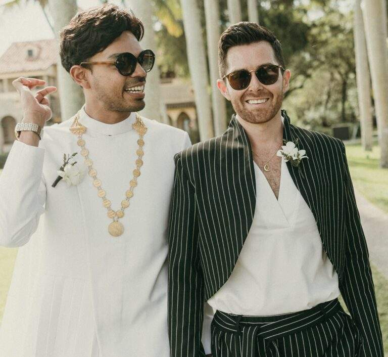 Grooms strolling down Deering Estate's Royal Palm Grove while smiling and conversing
