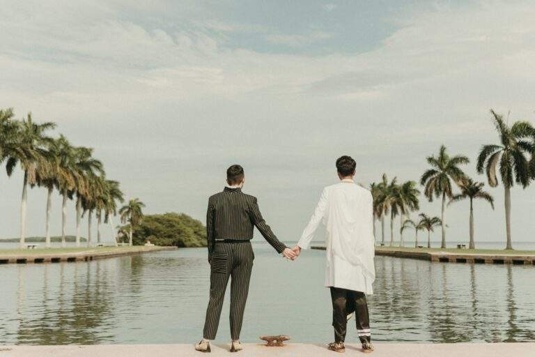 Grooms at Deering Estate's waterfront boat basin looking away from the camera towards Biscayne Bay while holding hands