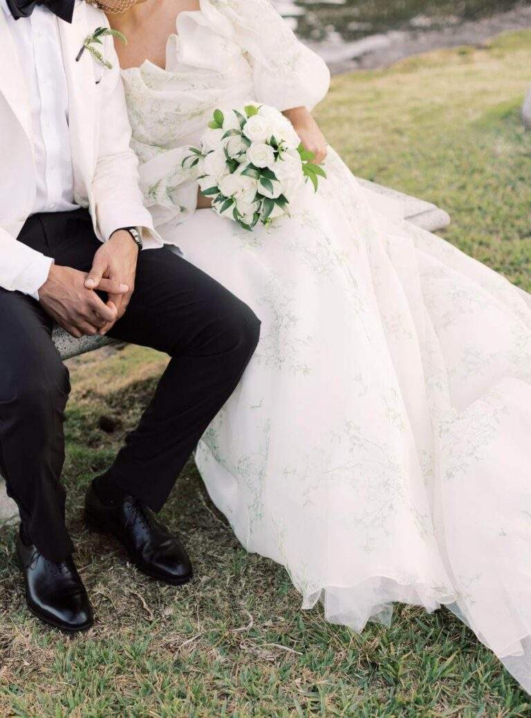 Couple seated at a bench with the focus on the bride's dress and bouquet