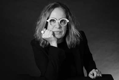 A woman dressed in black looks sternly into the camera.