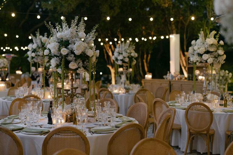 Tables and table setting decorated with lights and large white floral centerpieces set for a wedding reception.