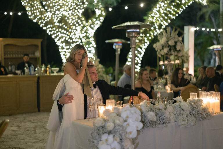 A bride being held by her groom as she wipes tears away from her face during the reception of their wedding.