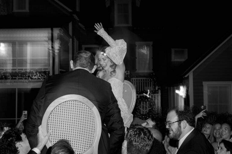 A bride and groom are lifted on chairs by celebrants at their wedding.