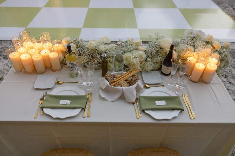 The bride and groom's table setting with candles, florals, a basket of bread, bottles of wine, wine glasses, plates, and golden silverware.