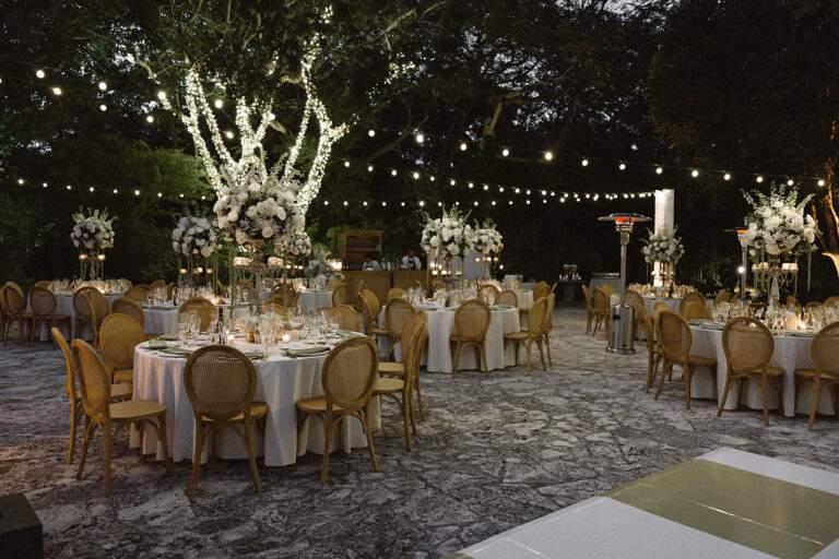 Tables and table setting decorated with lights and large white floral centerpieces set for a wedding reception.