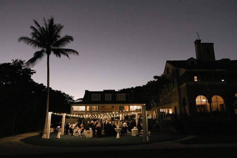 The lawn area in front of the Richmond Cottage decorated with string lights and high top tables for a cocktail hour. The lawn area is filled with wedding guests.