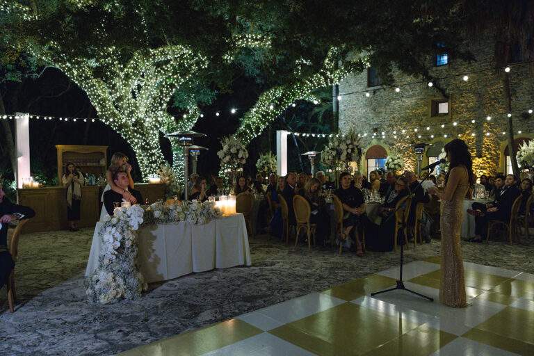 A bride and groom watch as a family member gives a speech during their wedding reception at Deering Estate.
