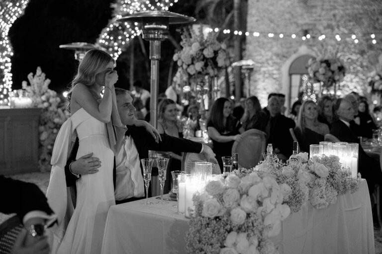 A bride being held by her groom as she wipes tears away from her face during the reception of their wedding.