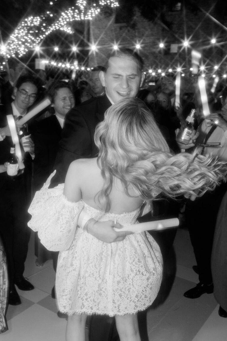 A bride and groom dancing joyfully at their wedding reception surrounded by their loved ones.