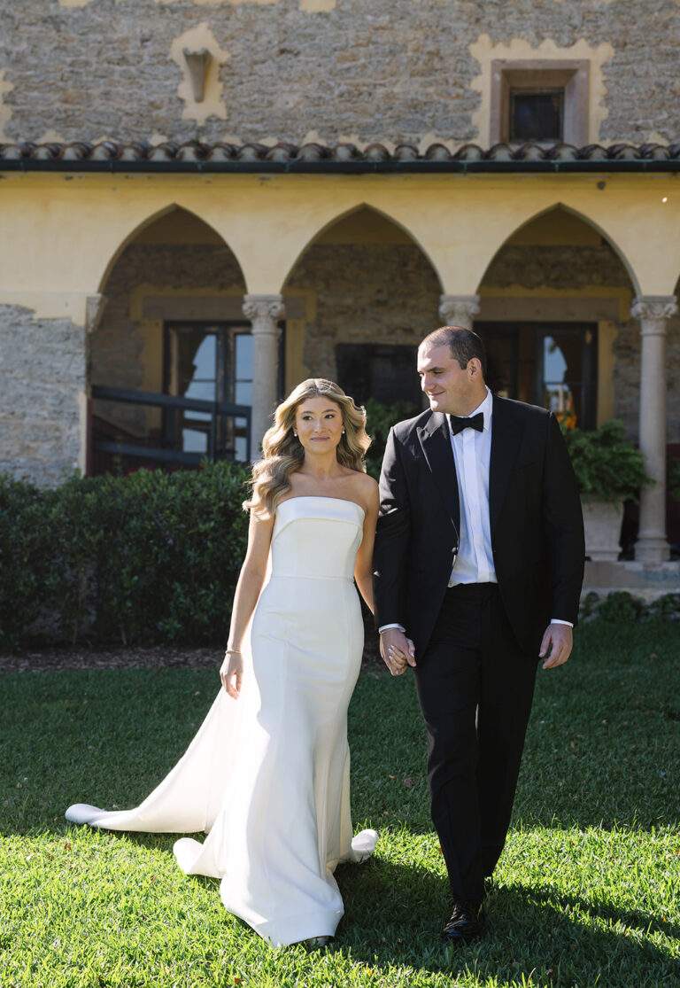 A bride and groom walk away from the Stone House hand-in-hand. As the bride looks off to the side, the groom is looking lovingly at the bride.