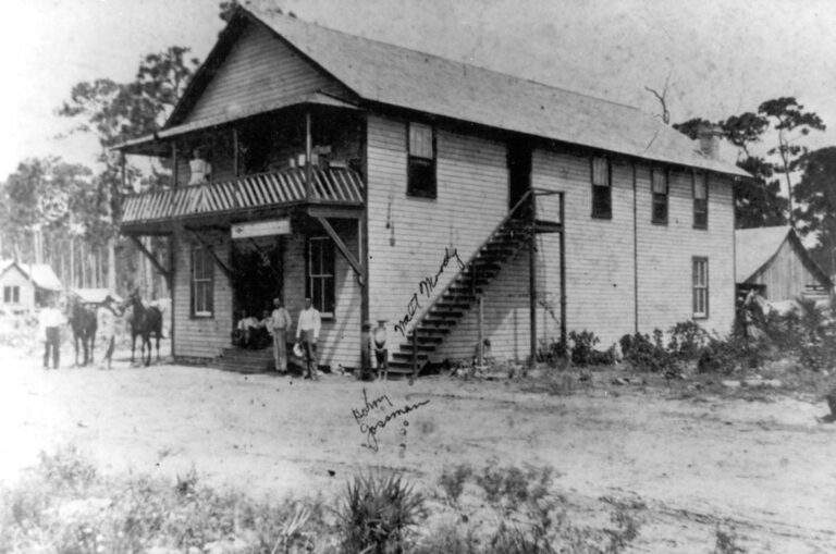 Historic photograph of a two-story panel sided building, the Brown & Moody General Store, one of several main town buildings along with a post office, factory, and school serving over 75 settlers