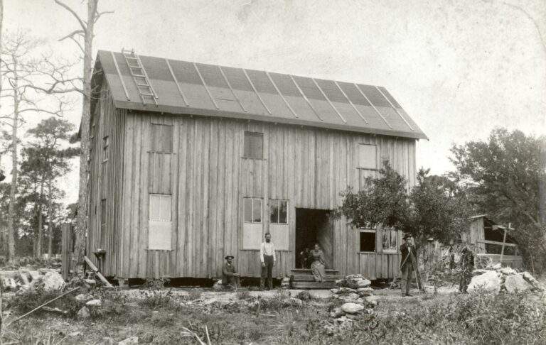 Dr. Samuel Richmond, land surveyor of the Florida East Coast Railway company, and his wife Edith Richmond standing in front of their home as it was first built. Other surveyors with land surveying equipment also pose in the photo.
