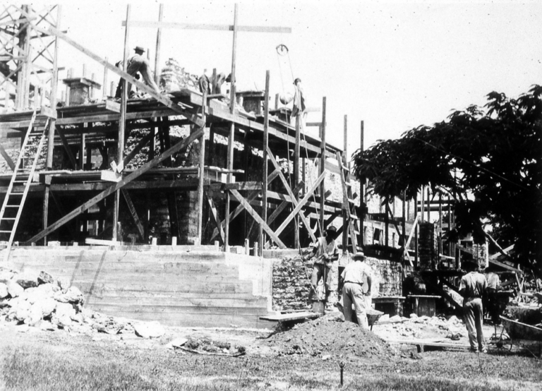 Builders working on Charles Deering's Stone House in the early 1900's, raising supplies up to the top level of scaffolding using a rope and pulley system.