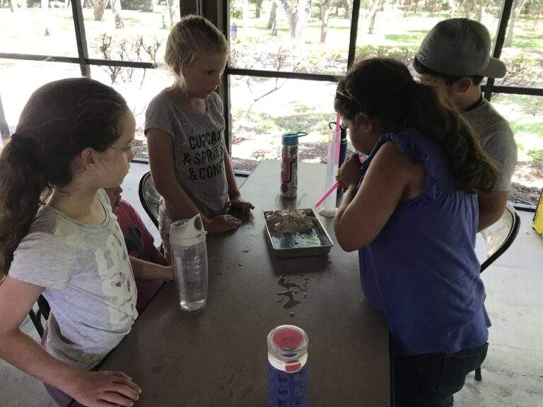 Campers working together on a project about erosion using cups of water to simulate rain and blown air through straws to simulate wind.