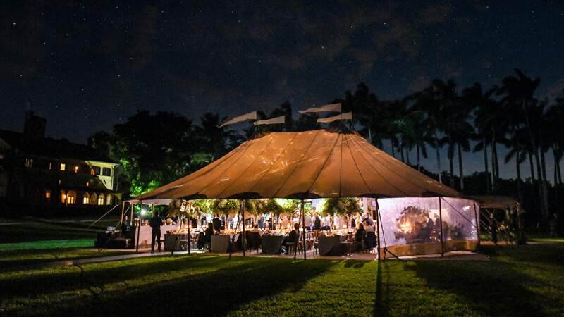 Night time wedding reception taking place under a large tent on the main lawn of Deering Estate