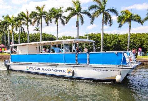 A white boat with blue sides named the Pelican Island Skipper departs from the Deering Estate boat basin.