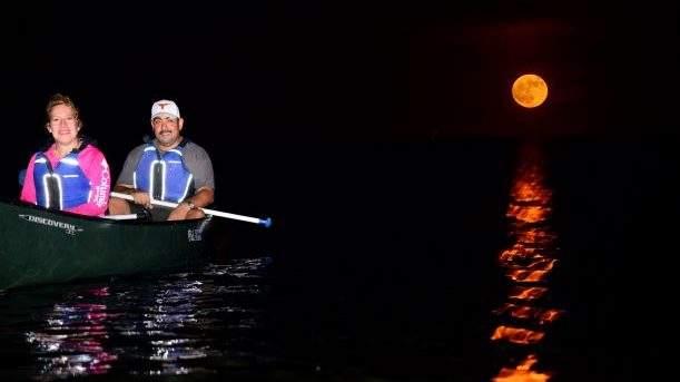 Two people in a canoe on Biscayne Bay at night with the full moon shining above them.