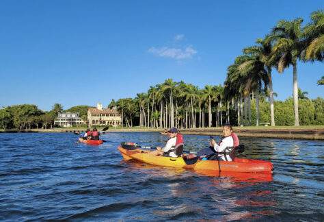 Deering Estate guests kayaking in the Boat Basin of Deering Estate with the historic homes in the background while on a historic tour of Biscayne Bay.