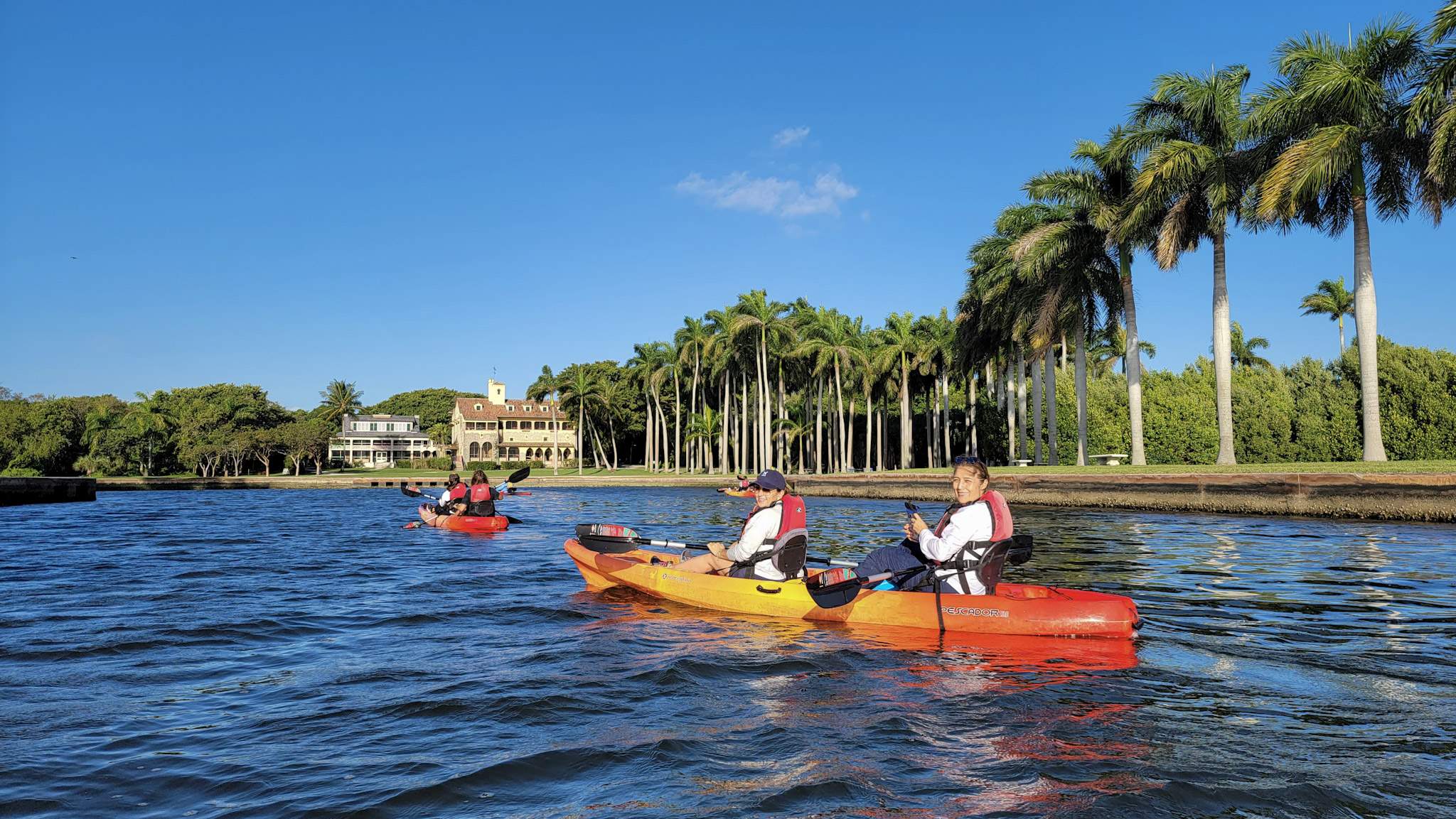 Deering Estate guests kayaking in the Boat Basin of Deering Estate with the historic homes in the background while on a historic tour of Biscayne Bay.