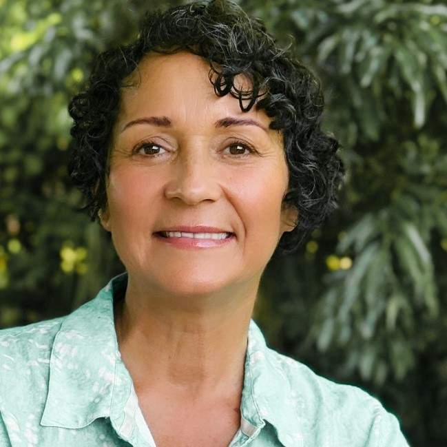 A woman with short, black, curly hair wearing a green collared shirt smiling at the camera. This is artist Aida Tejada.