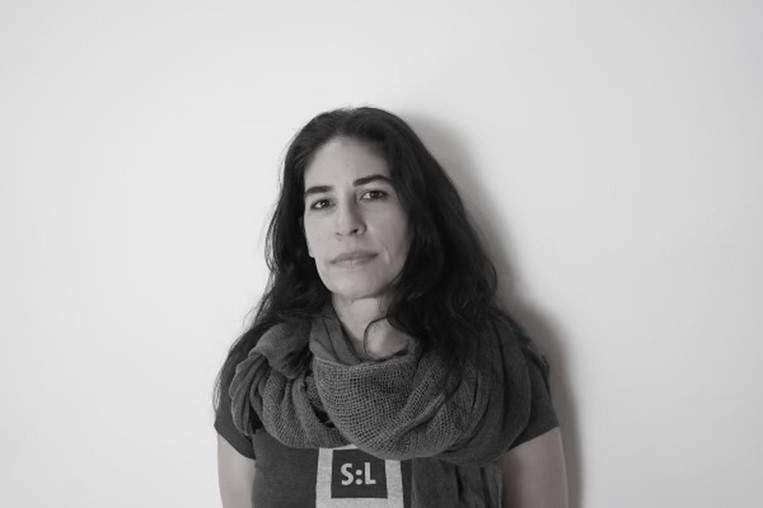 A black and white image of a woman with long black hair wearing a knit scarf and t-shirt looking at the camera. This is artist Natalia Garcia-Lee.
